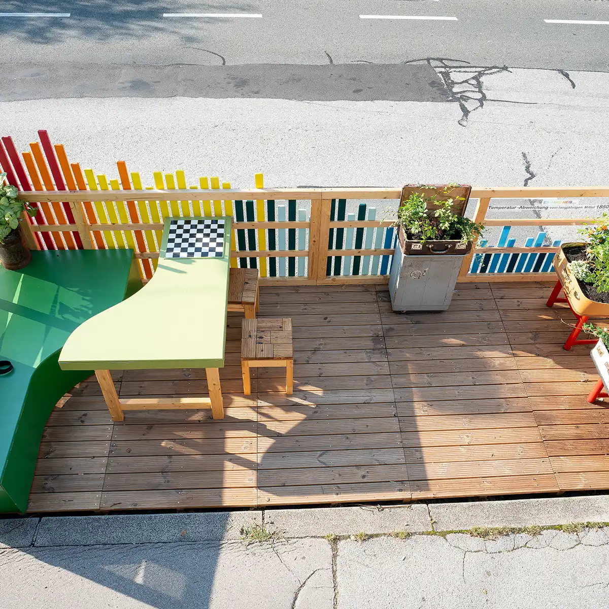 Parklet Begegnungszonen in Salzburg, die zum gemeinsamen Reden einladen: eine Holzterrasse, mit buntem Zaun und Sitzöglichkeiten, sowie Tischen