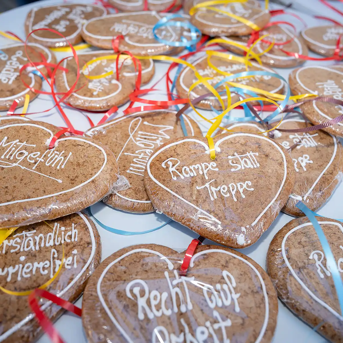 Lebkuchenherzen liegen auf einem Tisch, auf ihnen stehen Wörter wie Mitgefühl, Recht und Rampe statt Treppe. Sie tragen bunte Bänder