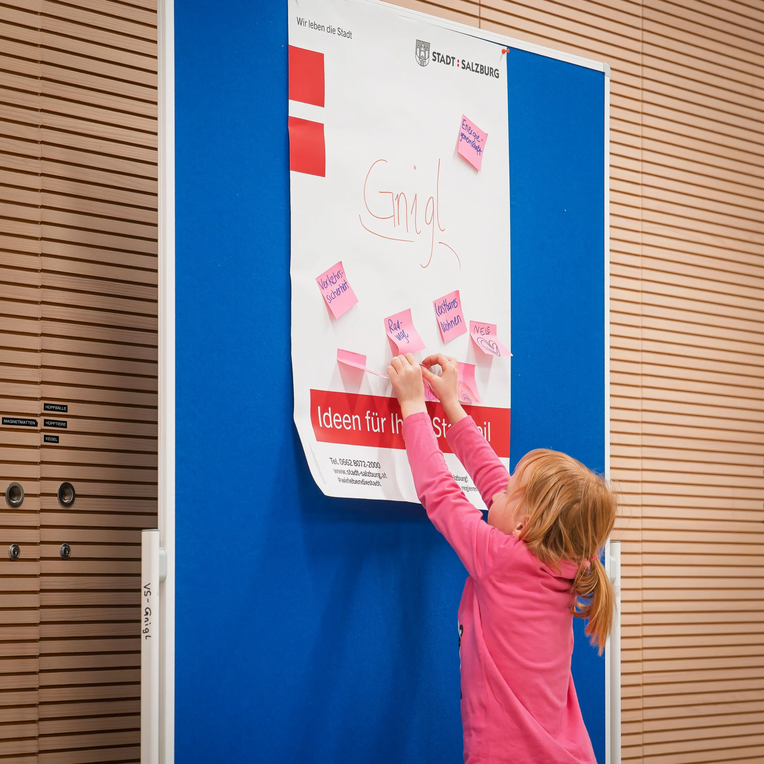 ein Mädchen klebt pinke beschriftete Post it's auf ein Flip Chart der Stadt Salzburg