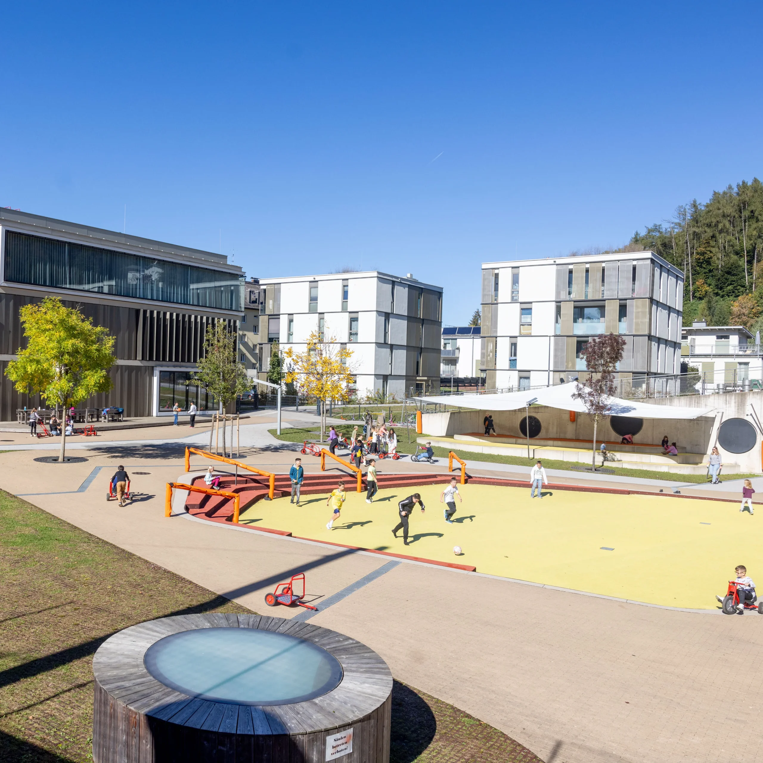 Bewegungsbereich im Bildungscampus Gnigl; Menschen spielen Fussball und fahren mit Kinder Fahrzeugen