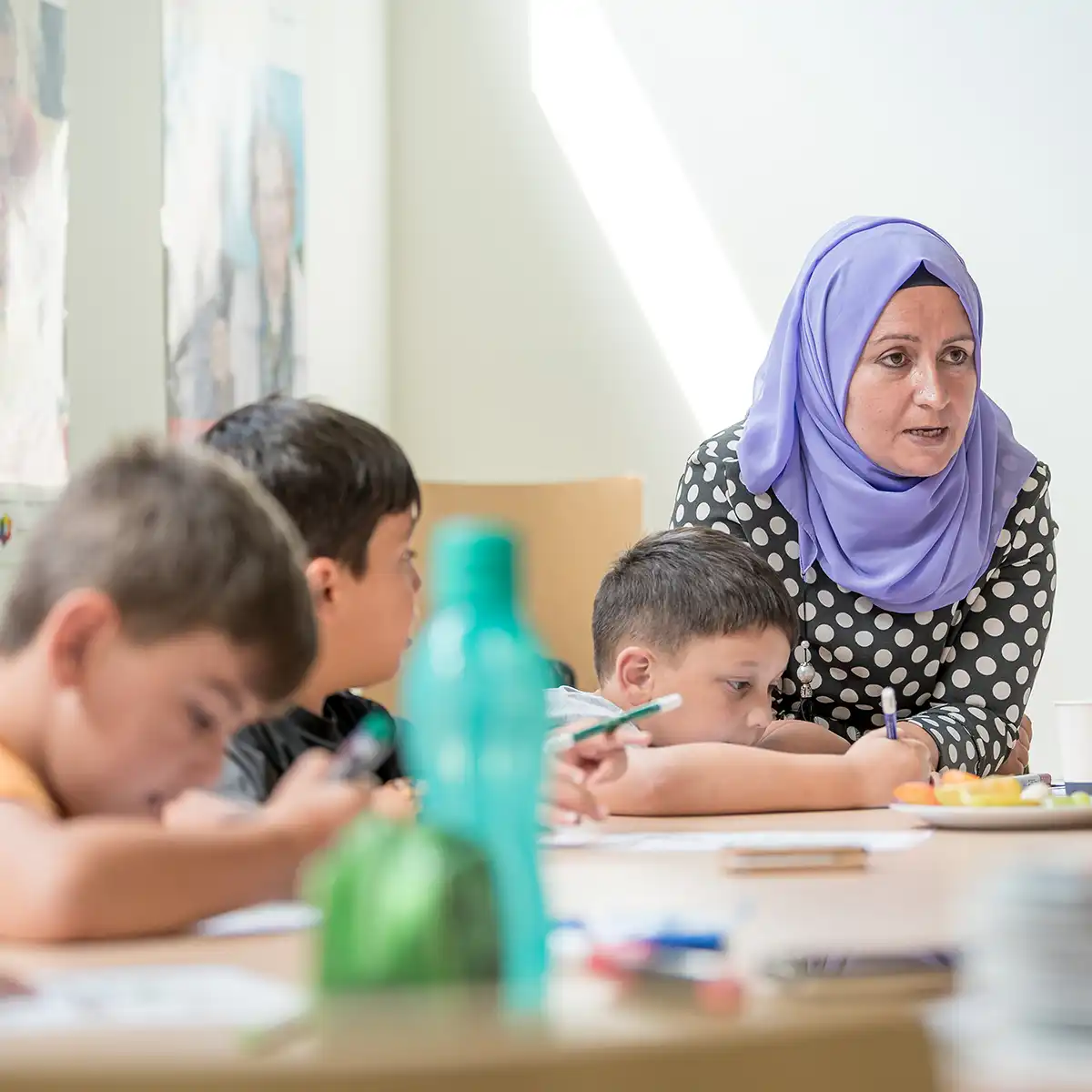 Eine Dame mit Kopftuch betreut Kinder, die am malen oder schreiben sind