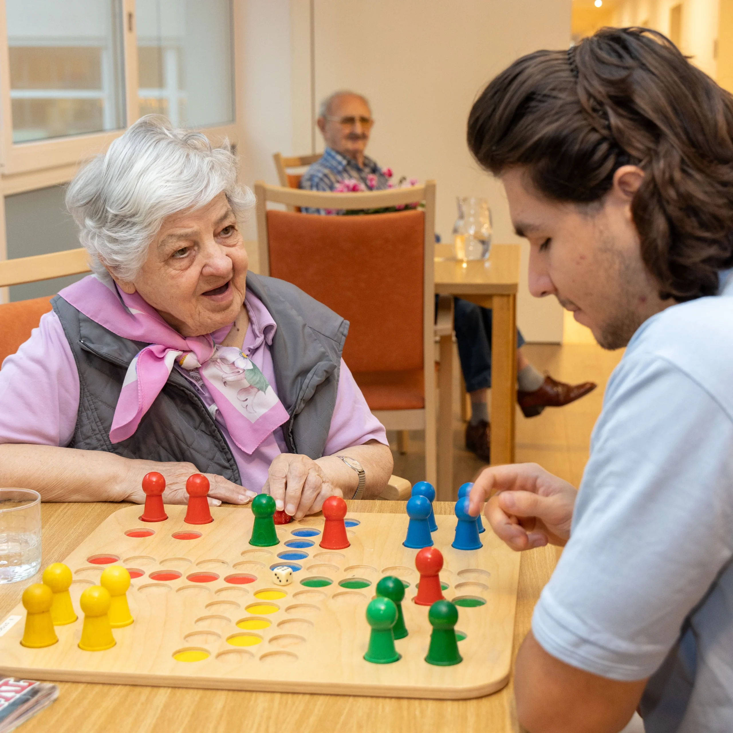 ein junger Pfleger spielt "Mensch ärgere dich nicht" mit einer Bewohnerin