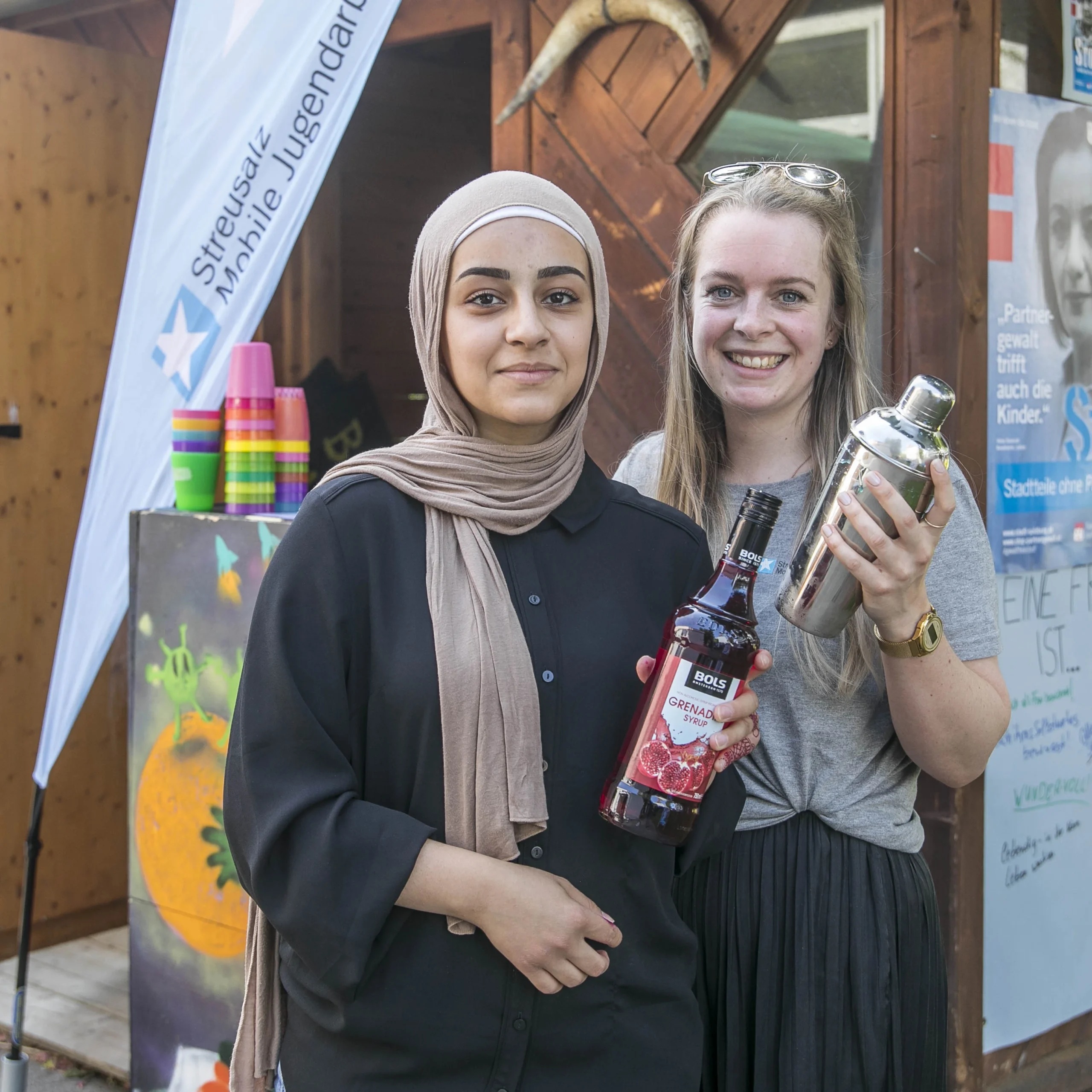 zwei Teenager Mädchen stehen mit Getränken in der Hand nebeneinander und haben sichtlich Spass