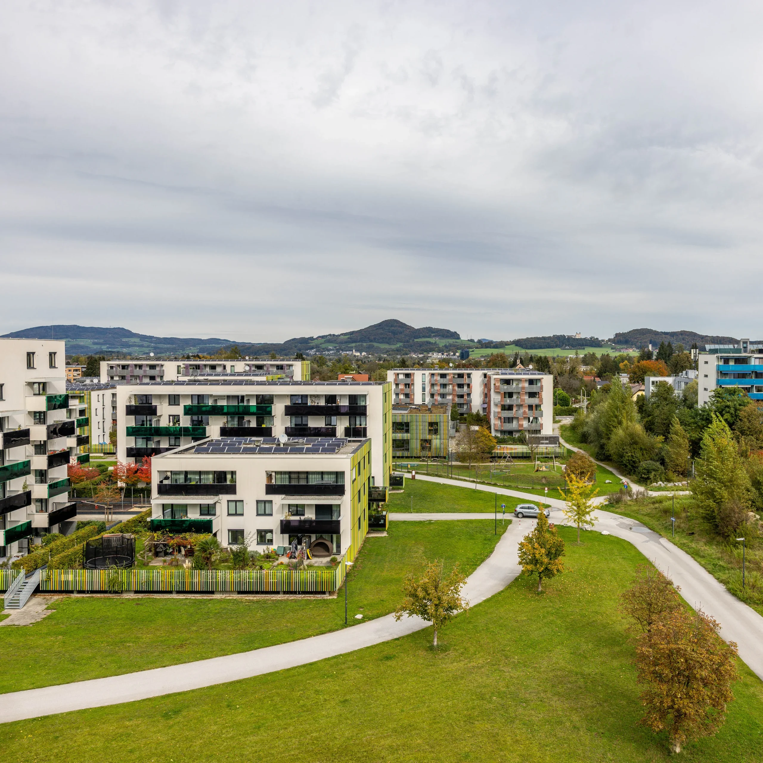 Ansicht von oben auf eine Siedlung mit vielen Gebäuden mit Zufahrtsstraßen und Wiesen, PV Anlagen auf den Dächern