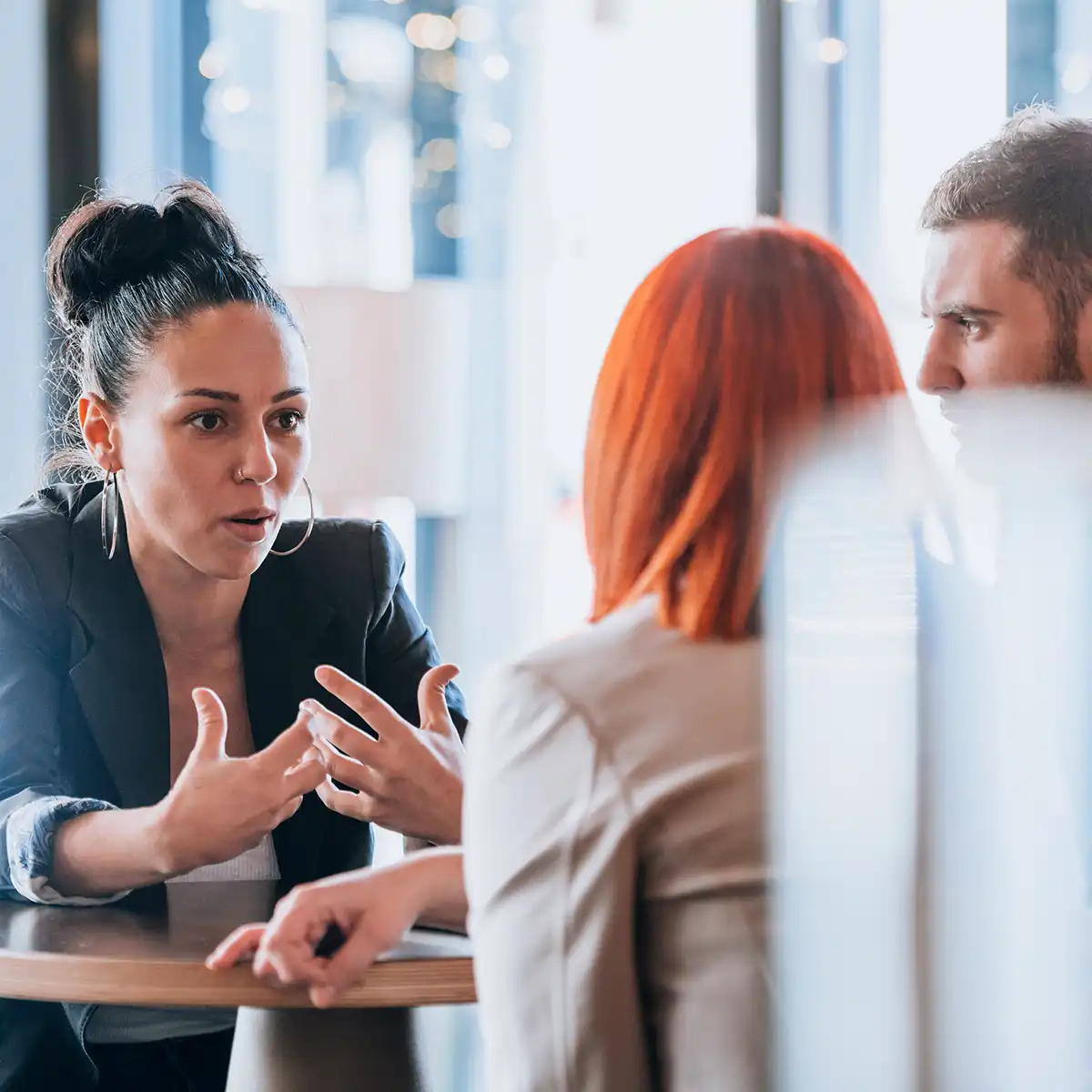 Drei Personen, die an einem Tisch ernst miteinander reden werden gezeigt